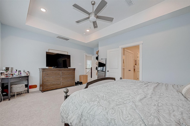 bedroom with ceiling fan, a raised ceiling, light carpet, and connected bathroom