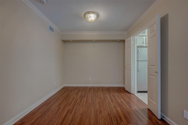 empty room featuring crown molding, light wood-type flooring, and a textured ceiling