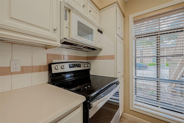 kitchen with light tile patterned flooring, tasteful backsplash, white cabinetry, and electric stove