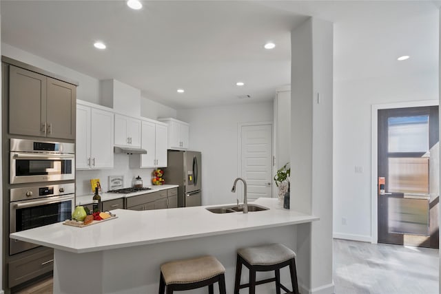 kitchen featuring gray cabinetry, sink, appliances with stainless steel finishes, kitchen peninsula, and a breakfast bar area