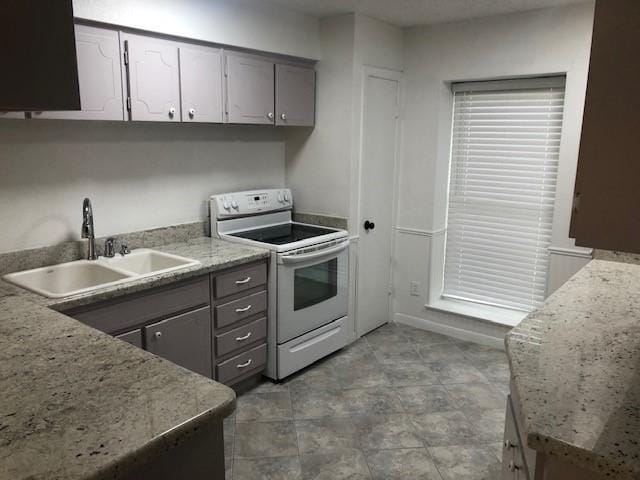 kitchen with white electric stove, gray cabinets, sink, and light stone countertops