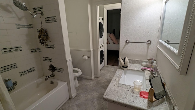 full bathroom featuring tiled shower / bath, stacked washer and clothes dryer, vanity, and toilet