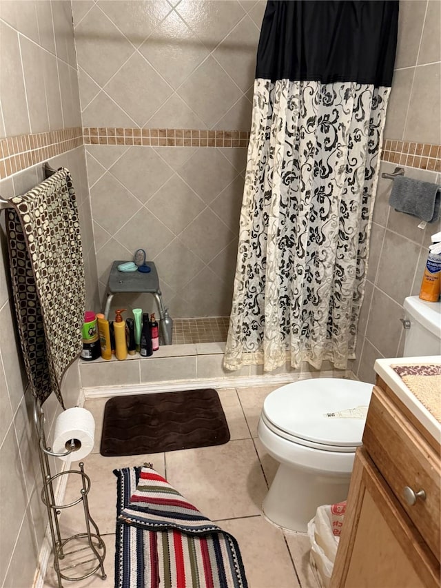 bathroom with tile patterned flooring, toilet, vanity, tile walls, and a tile shower