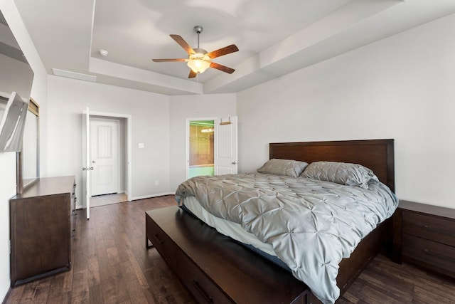 bedroom featuring ceiling fan, a raised ceiling, dark wood-type flooring, and connected bathroom