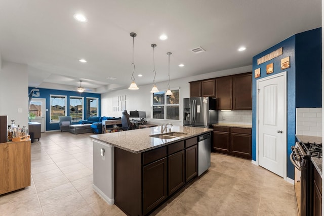 kitchen with light stone countertops, ceiling fan, sink, stainless steel appliances, and a center island with sink