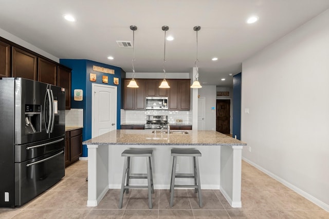 kitchen with a kitchen island with sink, hanging light fixtures, sink, decorative backsplash, and appliances with stainless steel finishes