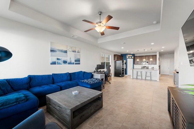 living room with a raised ceiling, ceiling fan, and light tile patterned flooring