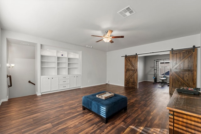 living room with built in shelves, a barn door, ceiling fan, and dark wood-type flooring