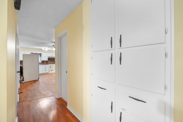 corridor with a textured ceiling and light hardwood / wood-style flooring