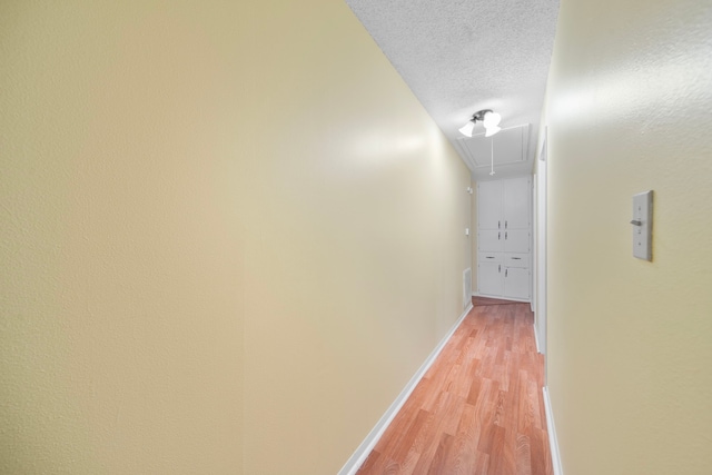 hall with light wood-type flooring and a textured ceiling