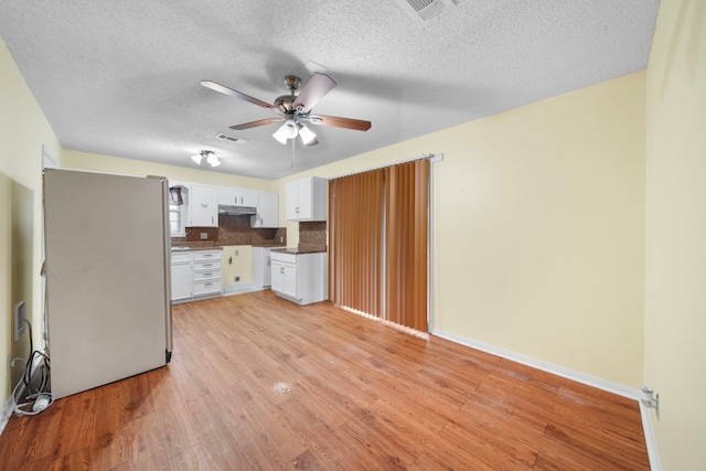 kitchen featuring backsplash, light hardwood / wood-style floors, a textured ceiling, white cabinets, and white fridge