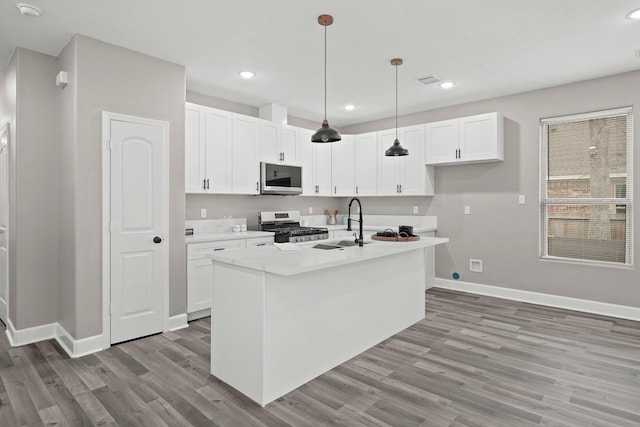 kitchen featuring white cabinets, light wood-type flooring, an island with sink, decorative light fixtures, and gas stove