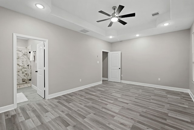 unfurnished bedroom featuring a tray ceiling, connected bathroom, ceiling fan, and light hardwood / wood-style flooring