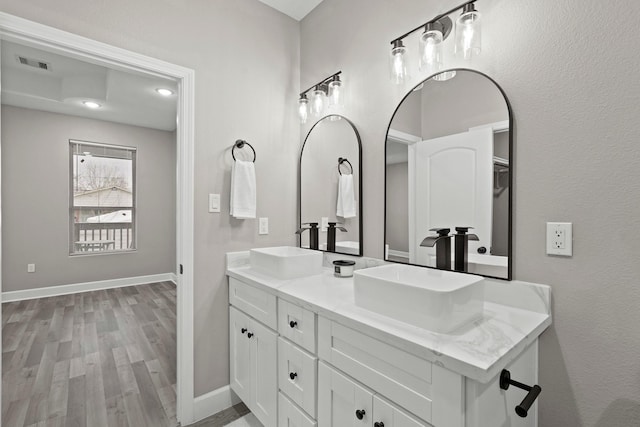 full bath with wood finished floors, visible vents, a sink, and double vanity