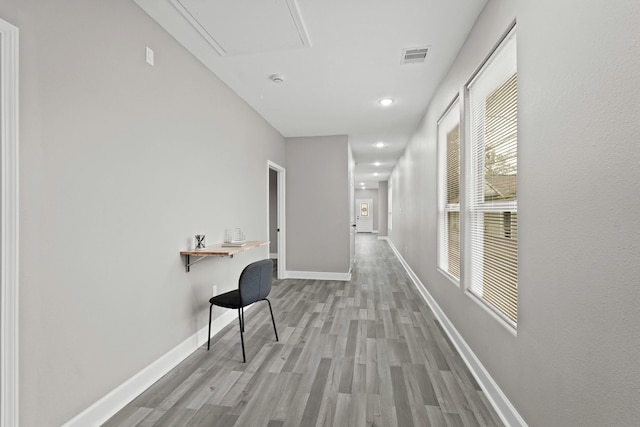 hall with attic access, visible vents, light wood-style flooring, and baseboards