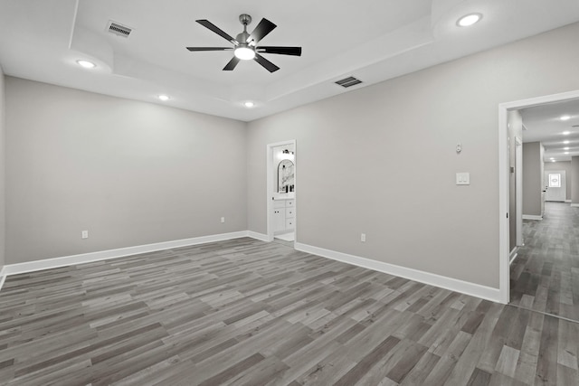 empty room with baseboards, a raised ceiling, wood finished floors, and recessed lighting