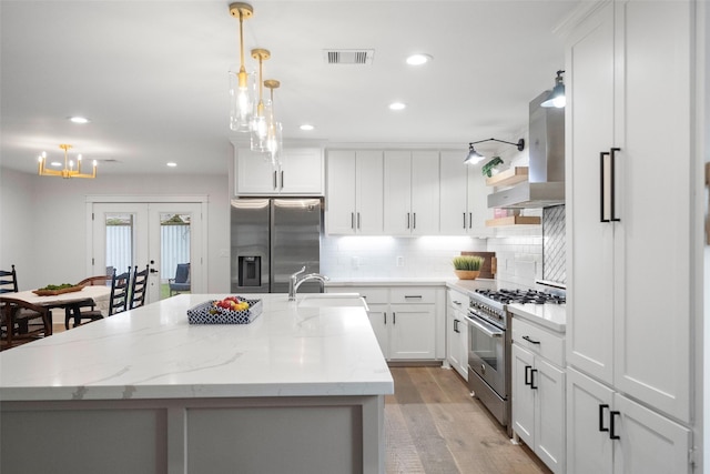 kitchen with white cabinetry, sink, hanging light fixtures, stainless steel appliances, and a center island with sink