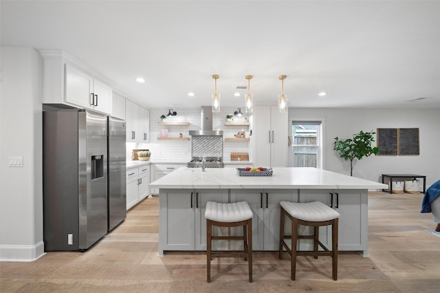 kitchen with wall chimney exhaust hood, a kitchen island, white cabinetry, and stainless steel refrigerator with ice dispenser