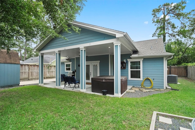 rear view of property with a hot tub, ceiling fan, a patio area, and a lawn