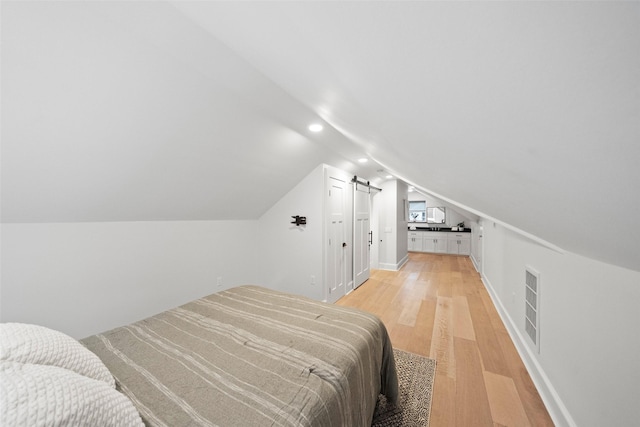 bedroom featuring a barn door, light hardwood / wood-style floors, and lofted ceiling