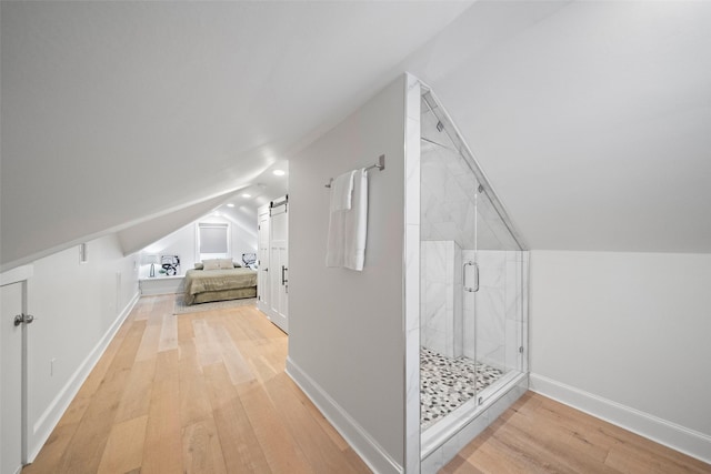 bonus room with a barn door, light hardwood / wood-style floors, and vaulted ceiling