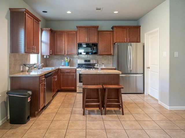 kitchen with sink, light tile patterned flooring, a breakfast bar area, a kitchen island, and appliances with stainless steel finishes