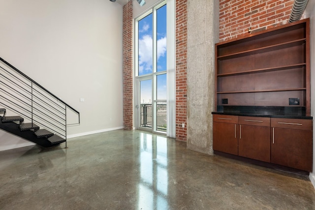 unfurnished living room with a high ceiling and brick wall