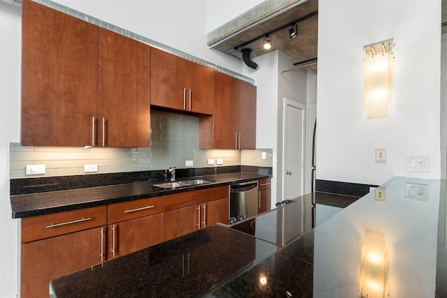 kitchen with dishwasher, dark stone counters, track lighting, sink, and decorative backsplash