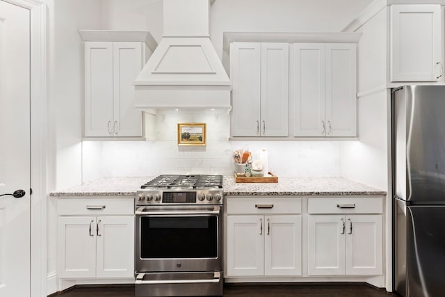 kitchen with light stone countertops, backsplash, custom range hood, stainless steel appliances, and white cabinetry