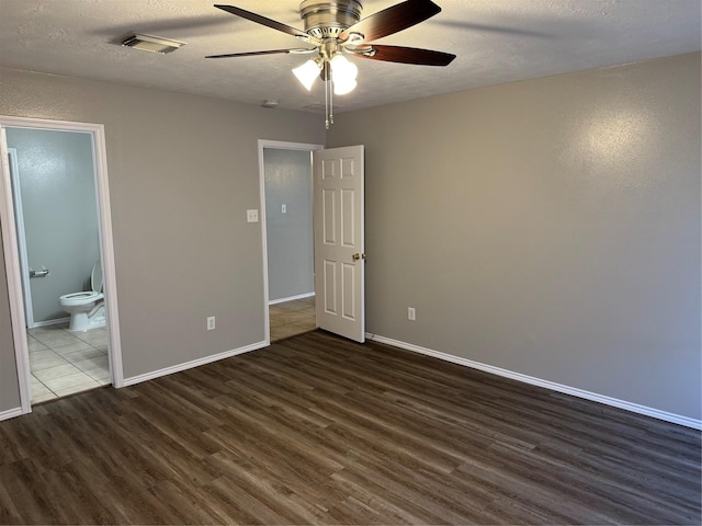 unfurnished bedroom featuring ceiling fan, dark wood-type flooring, ensuite bathroom, and a textured ceiling