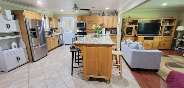 kitchen with appliances with stainless steel finishes, ornamental molding, a breakfast bar, ceiling fan, and light tile patterned floors