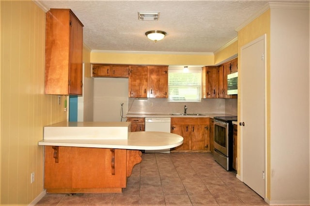 kitchen with kitchen peninsula, a textured ceiling, white appliances, crown molding, and a breakfast bar area