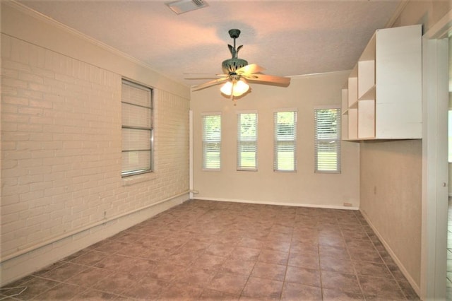 unfurnished room featuring ceiling fan, crown molding, and brick wall