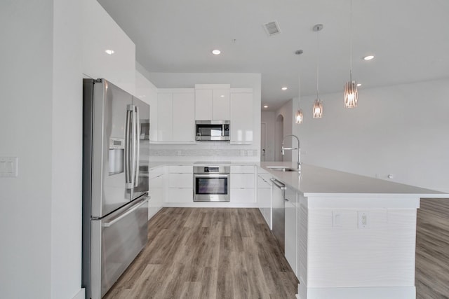 kitchen with pendant lighting, white cabinets, sink, an island with sink, and appliances with stainless steel finishes