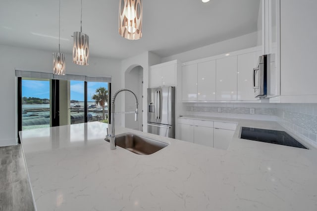 kitchen with white cabinetry, light stone counters, stainless steel refrigerator with ice dispenser, black cooktop, and pendant lighting