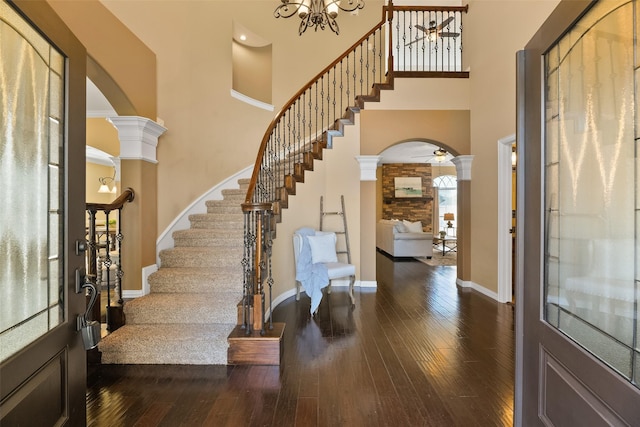 foyer entrance featuring decorative columns, dark hardwood / wood-style flooring, a towering ceiling, and an inviting chandelier