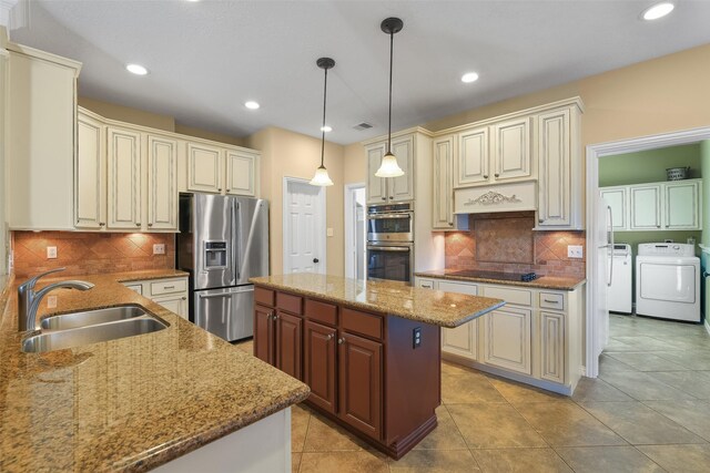 kitchen with pendant lighting, sink, a kitchen island, stainless steel appliances, and washing machine and clothes dryer