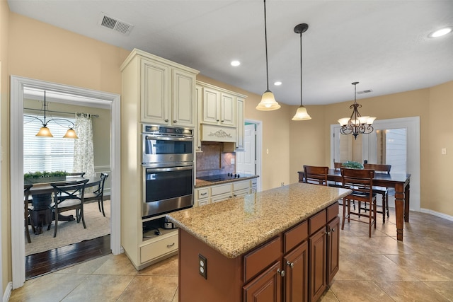 kitchen with double oven, cream cabinets, pendant lighting, an inviting chandelier, and a kitchen island