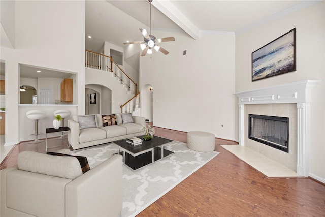 living room featuring ceiling fan, dark hardwood / wood-style floors, crown molding, a tile fireplace, and lofted ceiling with beams