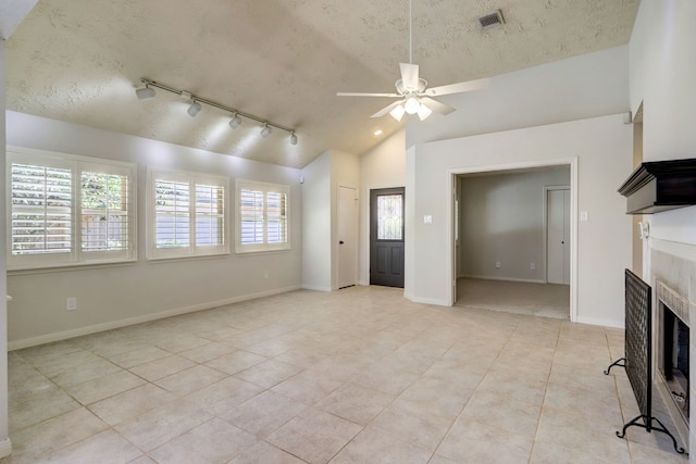 unfurnished living room with a wealth of natural light, rail lighting, ceiling fan, and lofted ceiling