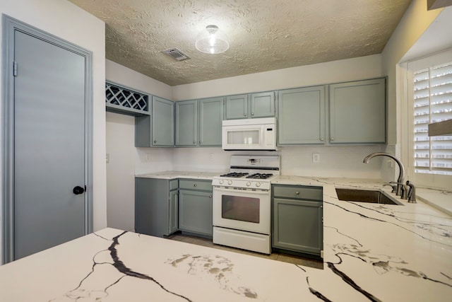 kitchen featuring a textured ceiling, light stone counters, sink, and white appliances