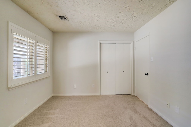 unfurnished bedroom featuring a textured ceiling, light colored carpet, and a closet