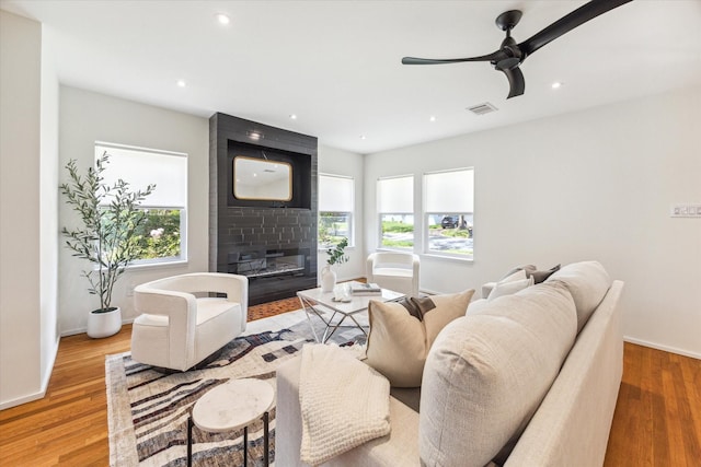 living room with a large fireplace, a wealth of natural light, light hardwood / wood-style flooring, and ceiling fan