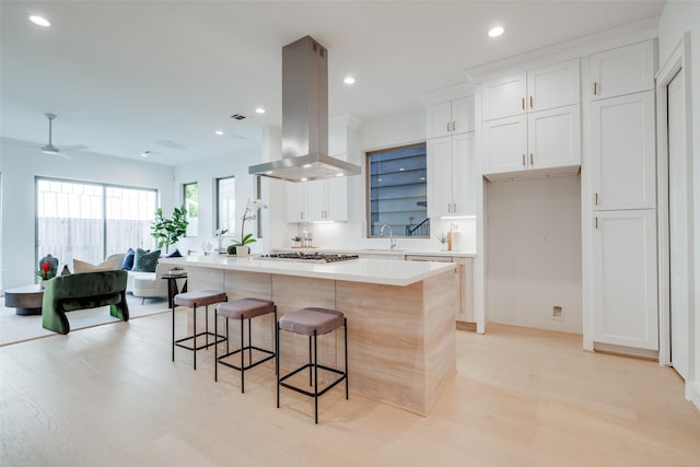 kitchen with a breakfast bar, a center island, white cabinets, ceiling fan, and island exhaust hood