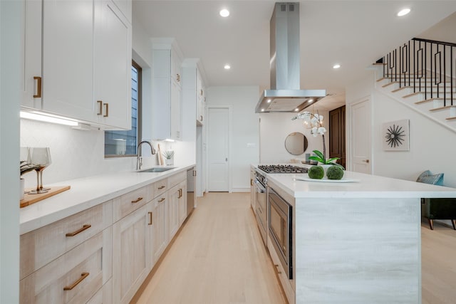 kitchen with island exhaust hood, stainless steel appliances, a kitchen island, sink, and white cabinetry