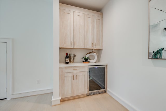 bar with decorative backsplash, light brown cabinetry, light wood-type flooring, and beverage cooler