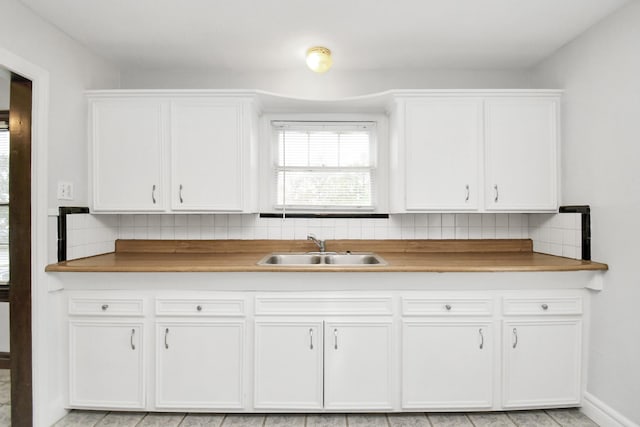 kitchen featuring butcher block counters, white cabinetry, sink, and tasteful backsplash