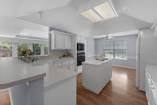 kitchen with kitchen peninsula, sink, black appliances, a center island, and white cabinetry