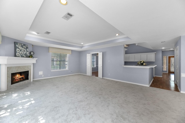 unfurnished living room with a high end fireplace, a tray ceiling, dark carpet, and ornamental molding