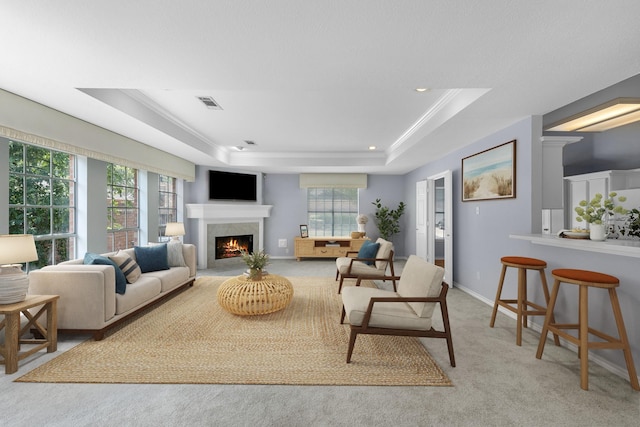 carpeted living room with a wealth of natural light, a raised ceiling, and a high end fireplace